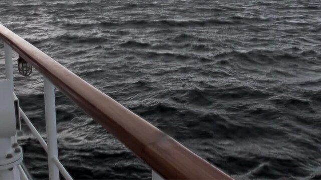 Ship glides gracefully across vast Arctic Ocean, its sturdy rail framing view of dark, undulating waves. This captures essence of tranquil yet powerful northern journey during daylight hours.