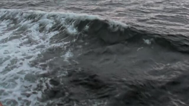 Experience the dynamic beauty of the Arctic Ocean. Powerful dark waves rise and fall, adorned with whitecaps, created by a ship's steady movement across the frigid northern waters.