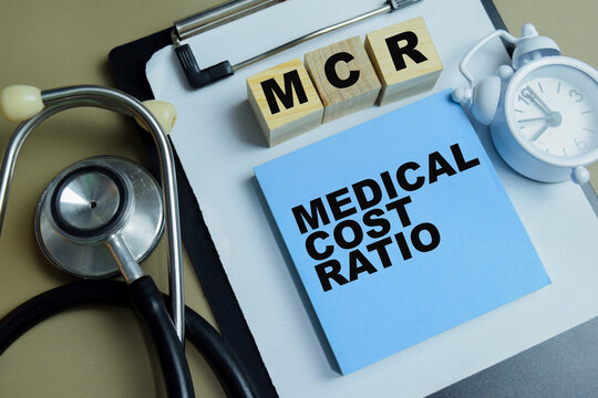 Concept of MCR - Medical Cost Ratio write on sticky notes isolated on Wooden Table.