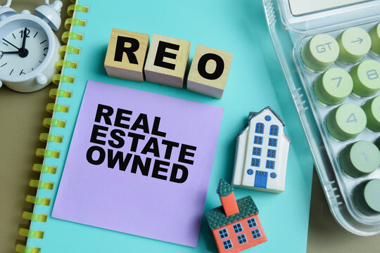 Concept of REO - Real Estate Owned write on sticky notes isolated on Wooden Table.