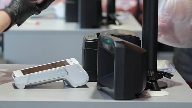 Hands in black gloves operating a modern payment terminal and scanner at a retail checkout counter