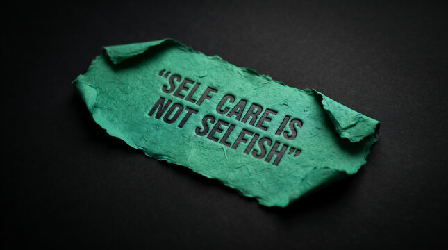 Green paper strip with embossed text self care is not selfish isolated on dark background conveying positive mental health affirmation for wellness and personal growth.