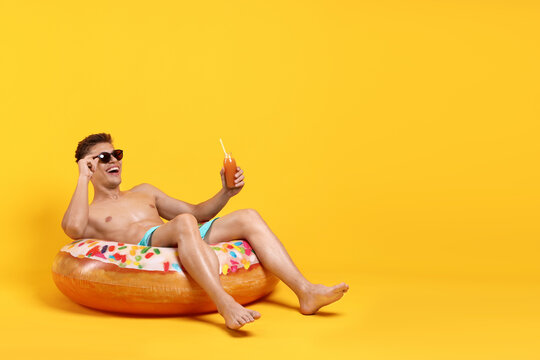 Man with drink and inflatable ring sunbathing on yellow background. Space for text