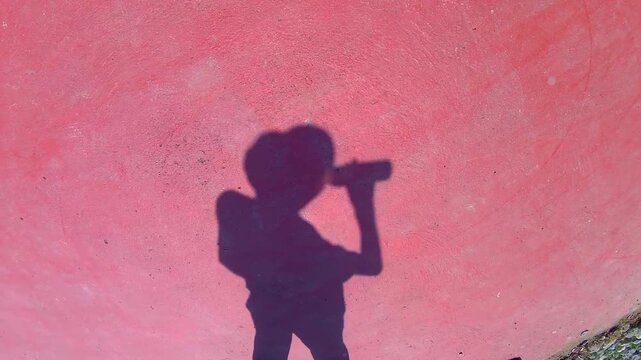 the shadow of a man in a Panama hat drinking from a bottle