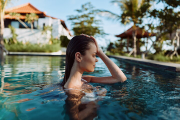Fototapeta premium Young woman relaxing in outdoor pool, enjoying sunny day, calm water, tropical background, peaceful moment, casual lifestyle, natural light, serene atmosphere