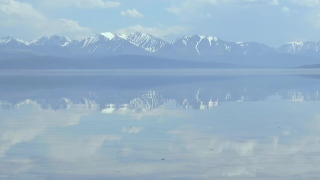 Experience the serene splendor of Lake Khuvsgul Mongolia. Majestic snow clad mountains and a boundless sky, adorned with gentle clouds, reflect exquisitely on the vast, tranquil lake. A perfect day.