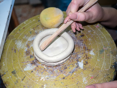 A professional potter expertly wielding a wooden modeling tool to seamlessly blend a fresh clay coil into a sturdy base demonstrating essential handbuilding skills in traditional ceramic crafting.