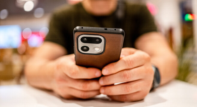 Man typing messages on mobile device during daylight at local cafe