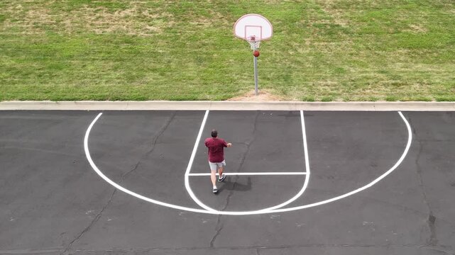 Aerial overhead view of middle-aged man shooting hoops on an outdoor basketball court for health, fitness, and active wellness at a public park