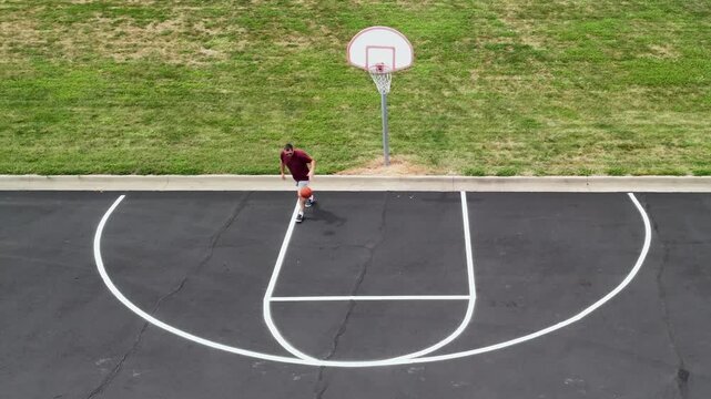 Aerial overhead view of middle-aged man shooting hoops on an outdoor basketball court for health, fitness, and active wellness at a public park