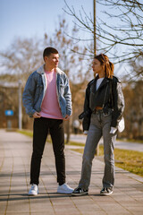 Obraz premium Young couple engaging in a conversation on a sunny day while walking along a paved pathway in an urban park setting