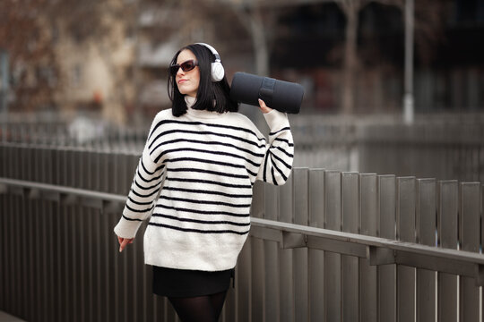 Girl dancing joyfully while wearing stylish headphones and a striped sweater in an urban setting during the afternoon, showcasing a vibrant moment of self-expression