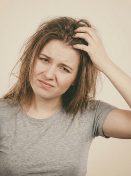 Young woman with messy hair scratching her itchy scalp. Frustrated female experiencing head irritation or dandruff against a plain background
