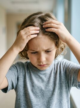 Young boy parting and inspecting his hair with a worried expression. Close up of child checking his scalp for head lice or nits