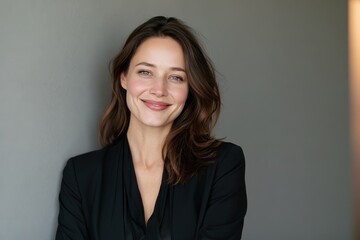 Obraz premium Confident smiling woman in smart casual attire posing beside a gray wall for a corporate portrait