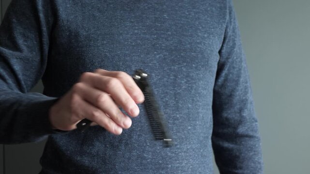 Adult male torso in blue sweater manipulating small black pocket knife near chest, visible action shows flicking, retracting, rotating, steady holding, and slight motion blur indoors