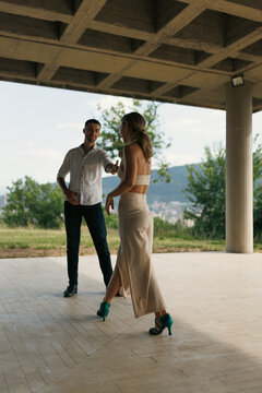 Young couple dancing outdoors under a concrete pavilion with scenic mountain view and summer romance in elegant attire