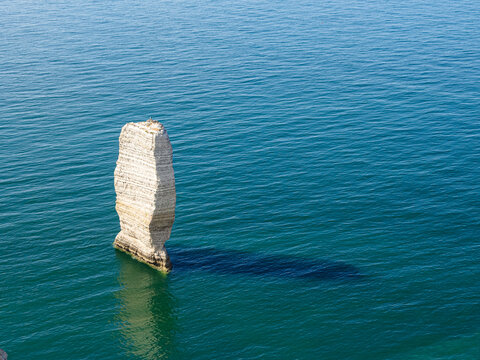 Vista de una roca blanca, alta y estrecha sobre el mar azul, en la costa de Etretat, viajando por la Normand&iacute;a Francesa en verano de 2022