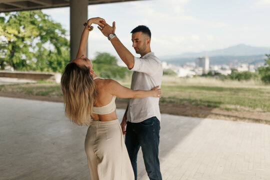 Romantic couple dancing outdoors under a pavilion sharing a slow dance with summer light and a distant city skyline