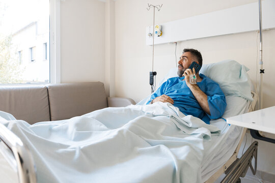 Patient man resting in hospital bed making phone call
