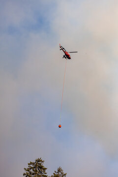 Firefighting Helicopter Carrying Bambi Bucket Over Forest Smoke Near Hope, BC, Canada