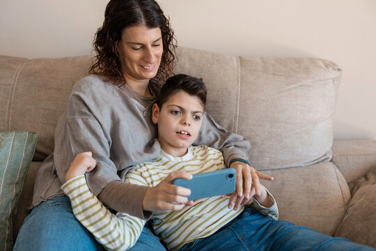 Mother and son relaxing on sofa using smartphone
