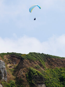 Parapentista desdendiendo del cielo azul sobre los acantilados verdes de la costa de Normand&iacute;a en Francia, viajando en verano de 2022