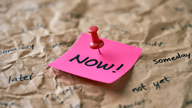 Bright Pink Note with "NOW!" Pinned to Crumpled Paper Amidst Phrases Like "Someday" and "Later"