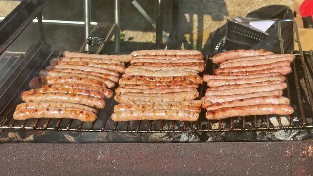 Rows of pork sausages cooking and smoking on hot outdoor barbecue grill rack