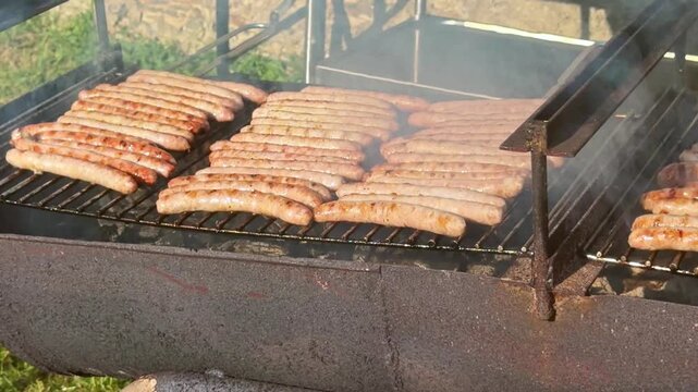 Row of pork sausages cooking and smoking on hot outdoor barbecue grill rack