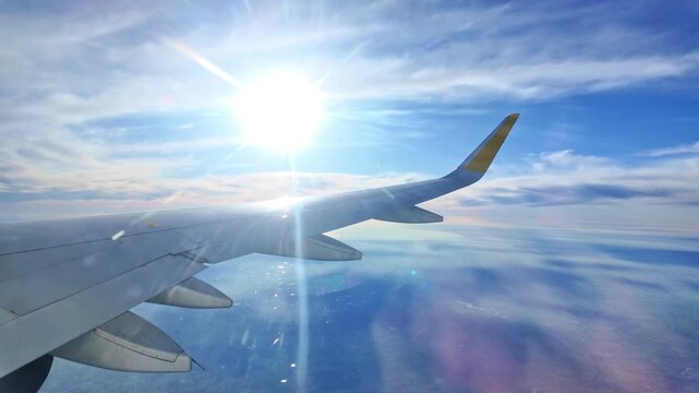 Bright sunlight and lens flare over airplane wing seen through cabin window during flight. Copy space
