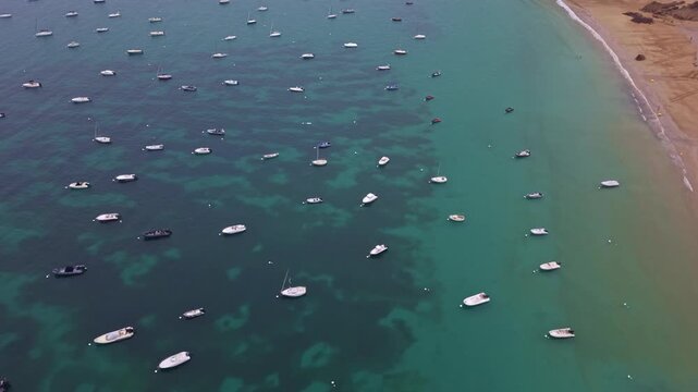 Perspective drone shot of densely parted boats anchored across the calm turquoise bay along sandy coastline at Saint-Lunaire, Bateaux, Brittany, France