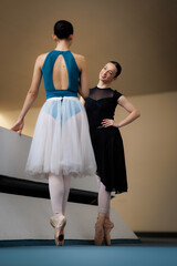 Ballet teacher coaching a ballerina on pointe during rehearsal in a dance studio, two dancers...