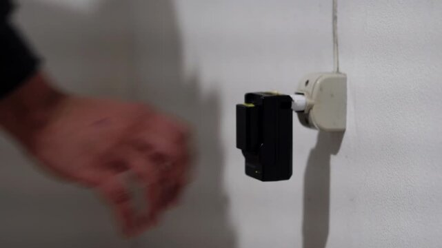 Latino man plugging a household appliance into a wall electrical outlet at home