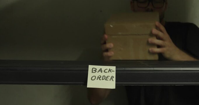 Warehouse worker removing the last package from a shelf marked with a backorder note. Ideal for inventory shortages, supply chain, logistics, and ecommerce concepts.