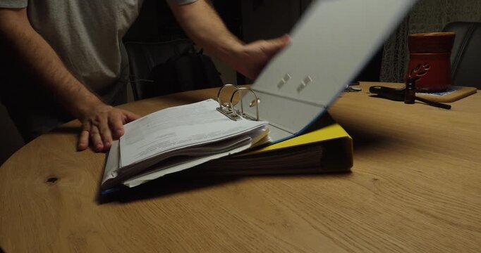 Man urgently searching through binders and documents for a missing paper. Ideal for lost files, paperwork stress and document management.