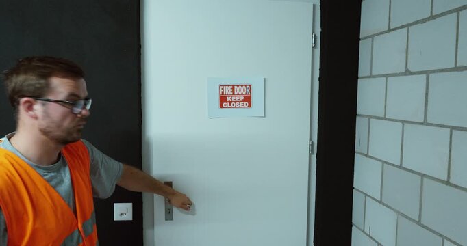 Worker attaching a Keep Fire Door Closed sign to a door. Ideal for fire safety, workplace regulations, emergency prevention and compliance.