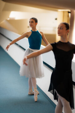 Two ballerinas practicing ballet en pointe in a sunlit rehearsal corridor, graceful dancers in tutus and leotards