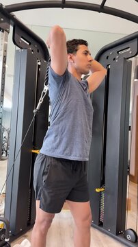 Strong man performing triceps extension exercises with rope attachment on cable machine