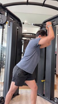 Man performs triceps cable pushdown exercise in modern indoor gym setting