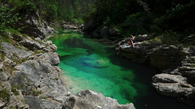 Persons resting on limestone rock above turquoise Pozze Smeraldine river pool. Meduna stream, Italy