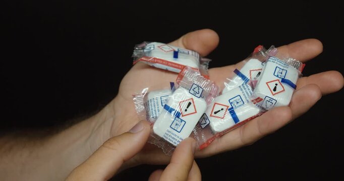Close-up of silica gel desiccant packets held in hand. Ideal for moisture protection, packaging, shipping, storage, and product preservation concepts.