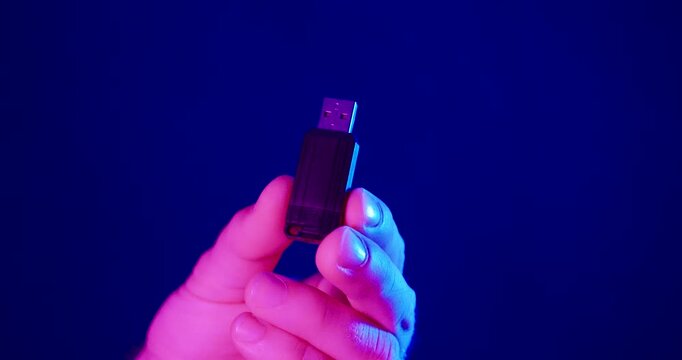 Close-up of a hand holding a USB flash drive under blue and pink neon lighting. Ideal for data storage, cybersecurity, file transfer, backup, digital privacy, and modern technology concepts.