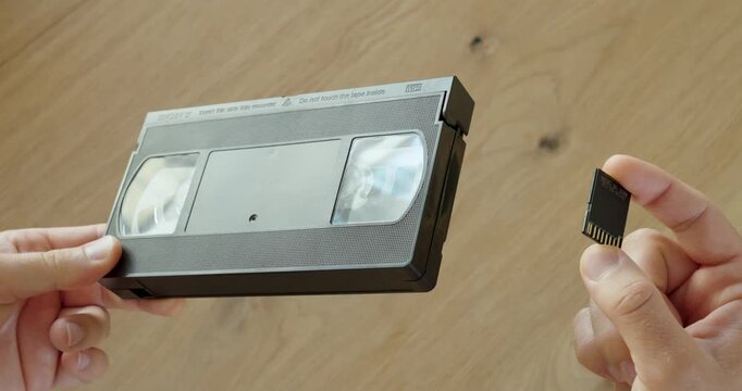 Person comparing an old VHS cassette with a modern SD memory card. Ideal for technology evolution, data storage, digitalization and retro media.