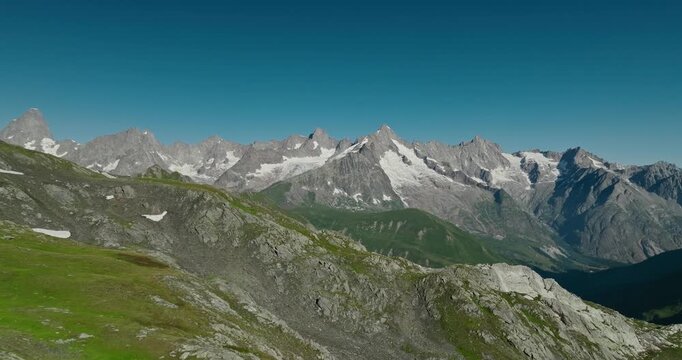 Drone flies above the dramatic terrain of Colle del Gran San Bernardo, revealing rugged alpine landscapes, snowcapped peaks and a crystal-clear blue summer sky on the Swiss&ndash;Italian border.