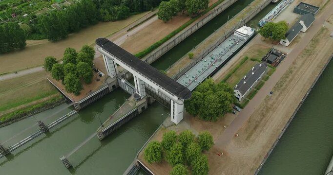 Overhead drone view of an industrial fluid barge leaving a lock chamber through an open sluice gate and continuing its journey along the canal.