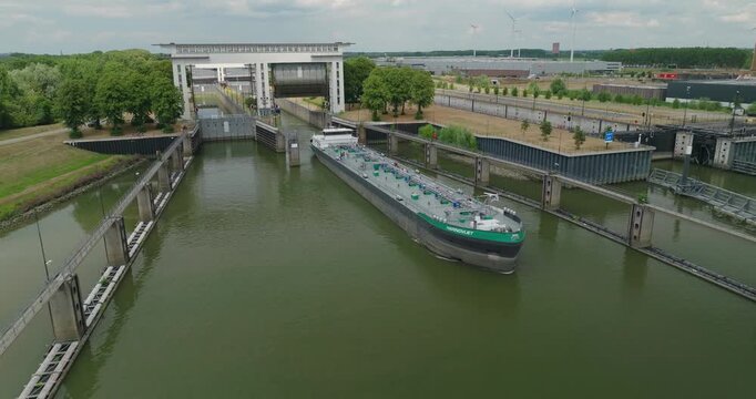 Drone flies ahead of an inland oil tanker barge after it passes beneath an open sluice gate, continuing its journey along the Dutch Lower Rhine River.