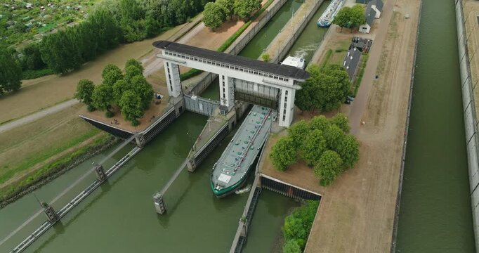 Drone footage of an inland oil tanker barge passing beneath an open sluice gate after leaving a lock chamber and continuing its journey along the canal.