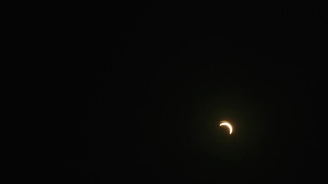 Timelapse of a partial solar eclipse during sunset, with the Moon covering part of the Sun as the crescent-shaped solar disc moves diagonally toward the horizon.