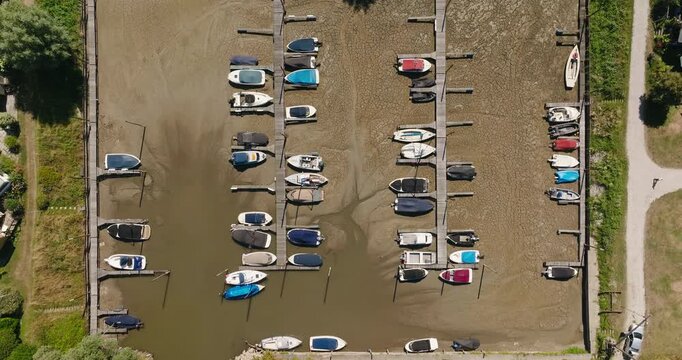Top down aerial view of a dried up harbor with stranded boats on the dock, while only the river mouth retains water and the surrounding soil is completely dry and cracked.